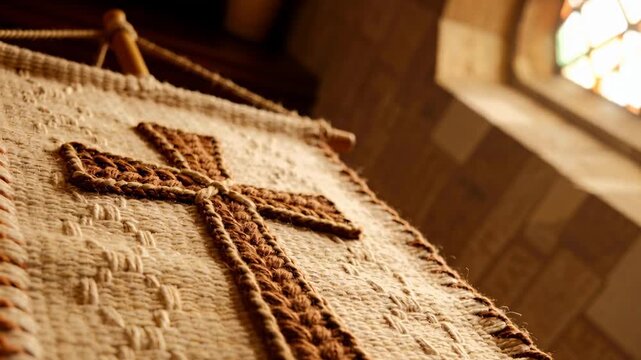 Tilting camera revealing embroidered braided cross on altar cloth in church, stained-glass light