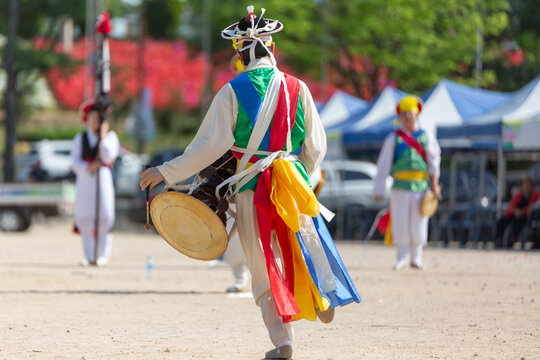 Traditional Korean pungmul performer playing janggu drum in colorful costume during an outdoor cultural festival.