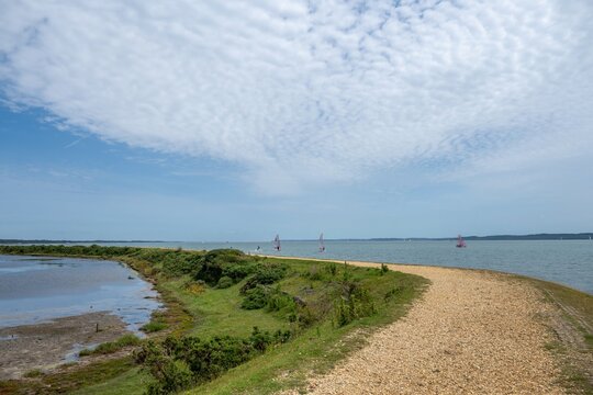 footpath along the Solent Way between Lymington and Keyhaven with the sea blue sky and wispy white clouds in the background