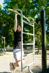 Obraz premium Vertical shot of woman hanging on street workout bars
