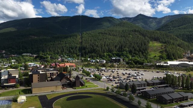 Aerial of small town development near Kellogg Idaho and Coeur Dalene National Forest in the late afternoon with scattered clouds with parking lots buildings and track and field