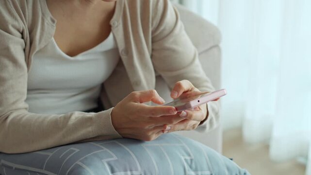 Young Asian woman relaxing and using mobile phone on a sofa at home in the morning
