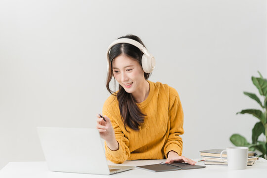 Virtual Learning Experience: A young woman with headphones immersed in online learning, joyfully engaging with her laptop, surrounded by study materials.