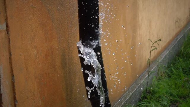 Stockholm, Sweden A leaky drain pipe in heavy rain spews out water onto the grass on the side of a house. 