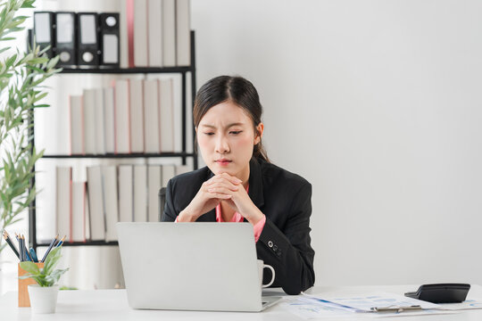 Concentration in Office: A young businesswoman sits at her desk, deeply focused on her laptop, with shelves of books and office supplies in the background.