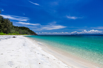 Obraz premium Koh Adang, Tarutao National Marine Park. White sandy beach meets turquoise Andaman Sea. Lush forested headland to the left. Clear sky and calm water.