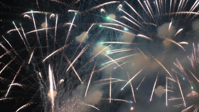 Detonating firework shells creating starburst bursts in open night sky for celebration, smoke haze