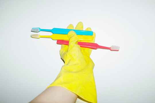 Hand holding colourful playful toothbrushes and wearing yellow glove