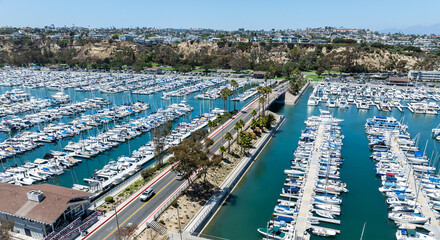 Fototapeta premium The California, Dana Point Harbor, with Bots and Yachts in their slips as people interact with the pacific ocean and sea cliffs in the background and sailboats