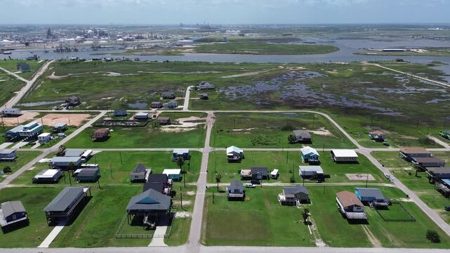 Marshside residential reach homes near Seashell Dr extend toward marsh corridor with refinery tanks pipelines rising beyond inland water channels. Varied roof colors, green parcels, Freeport, TX
