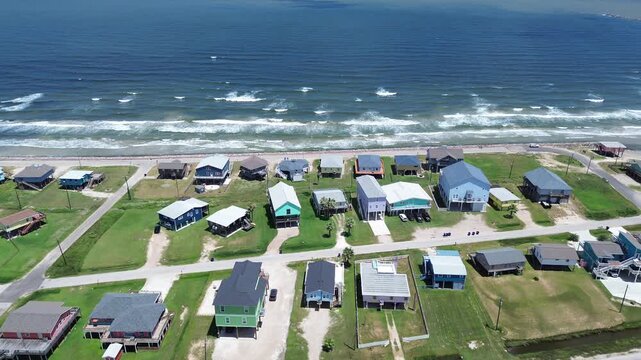 Shoreline parallel rows coastal homes near Seashell Dr align with sandy corridors running beside Gulf as elevated structures form continuous band along beach. Clean roof patterns, Freeport, TX