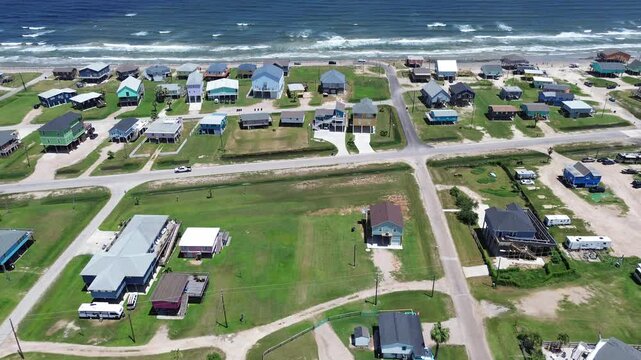 Coastal grid extension homes near Seashell Dr stretch toward Gulf shoreline with paved dirt roads forming tight neighborhood pattern beside beach corridor. Varied rooflines, grassy, Freeport, TX