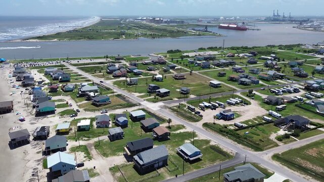 Portside coastal mix blocks near Seashell Dr sit beside RV pads elevated homes facing Gulf with clear views toward industrial port across inlet. Varied roof, vacation rentals, Freeport, Texas