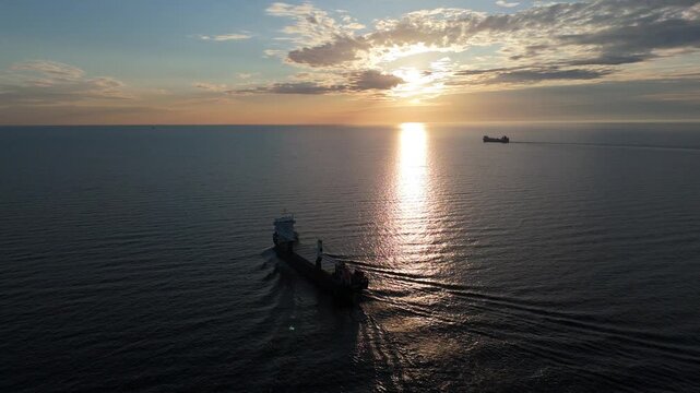 Scenic view of a cargo ship silhouette against the setting sun with long shadows on the water.