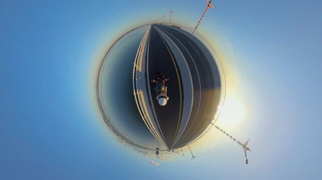 Little Planet View of Motorcycle Ride Across Southern Terminus of Bali Mandara Toll Road at Sunrise, Surrounded by Ocean, Highway and Clear Morning Sky