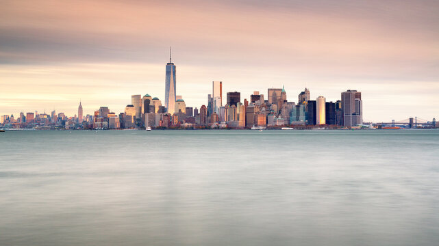 Manhattan skyline urban landscape rising above harbor waters at sunset offers an iconic travel destination background with extensive copy space, Lower Manhattan, New York City, USA.