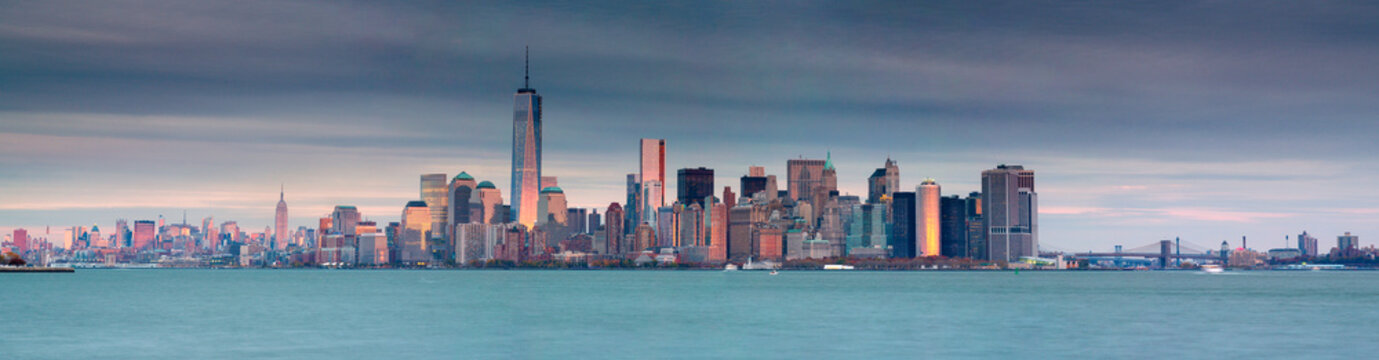 New York City skyline featuring towering skyscrapers reflecting warm light along the harbor at sunset, showcasing a vibrant tourism destination in Lower Manhattan, New York, USA.