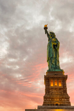 Statue of Liberty holds a glowing torch under a vibrant sunset sky, symbolizing freedom and travel at this iconic tourism destination on Liberty Island, New York City, USA.