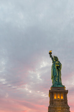 The Statue of Liberty stands against a vibrant sunset sky, serving as an iconic global symbol for travel, tourism, and history at Liberty Island, New York City.
