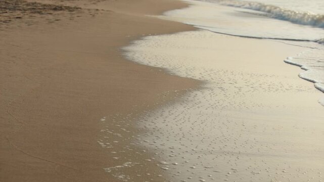 Advancing swell pushing white surf foam across wet glossy sand, showing rhythmic foreshore motion
