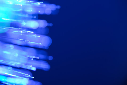 Glowing blue fiber optic tips creating bokeh barrier with large copy space on deep blue background.
