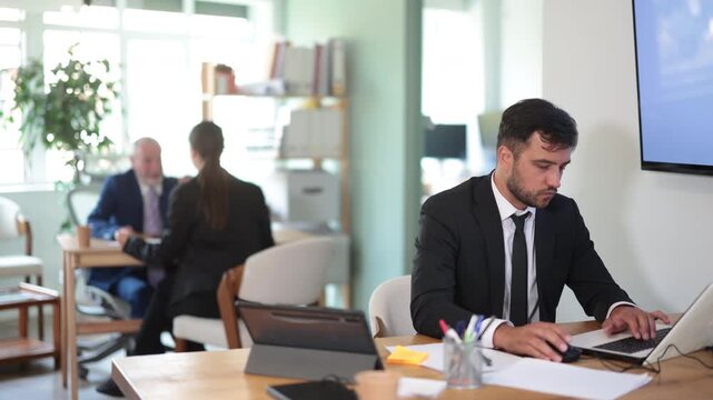 European man sits at a table in a bank office and checks electronic documents on a laptop. Office employee working on a laptop. High quality 4k footage
