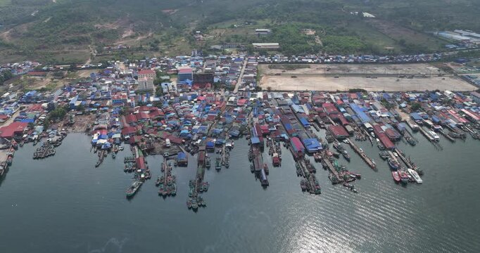 Panning aerial view of a densely populated fishing village, featuring rows of colorful houses and numerous boats docked along several long wooden piers.