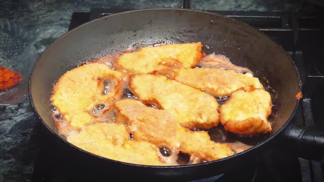 A close-up shot of seasoned, breaded chicken breast cutlets being pan-fried in hot oil on a stove, ideal for home cooking tutorials, recipe promotions, and culinary blogs.
