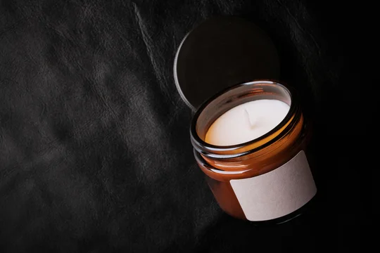 Scented candle in amber jar with white wax and blank label on black leather