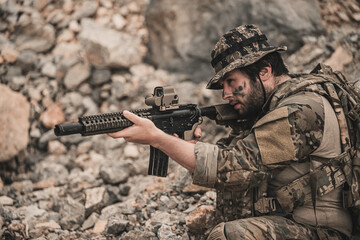 Obraz premium Exhausted military commando resting on rocky terrain during a combat mission. Tired armed forces operator catching his breath after battle. Tactical survival and warfare concept.