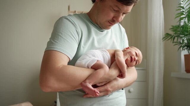 Caring father cradling his upset newborn son in his arms, gently trying to soothe the crying infant with gentle movements. Tender moment of paternal love, care, and family bonding
