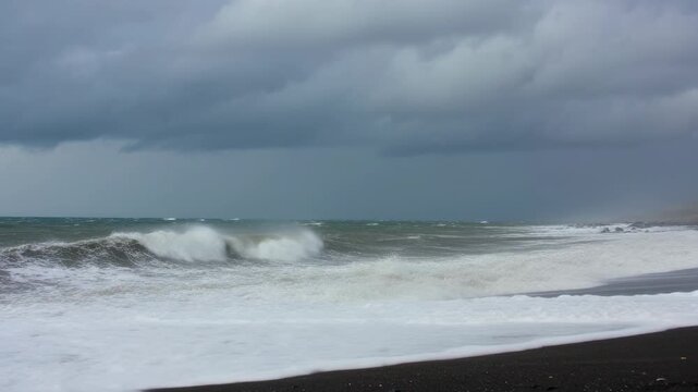 Surging surf cresting, breaking, washing white foam onto black sand beach driven by squall