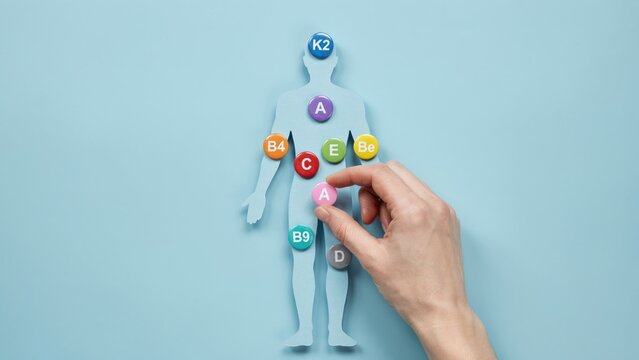 Hand placing vitamin a tablet on a human body silhouette, down view