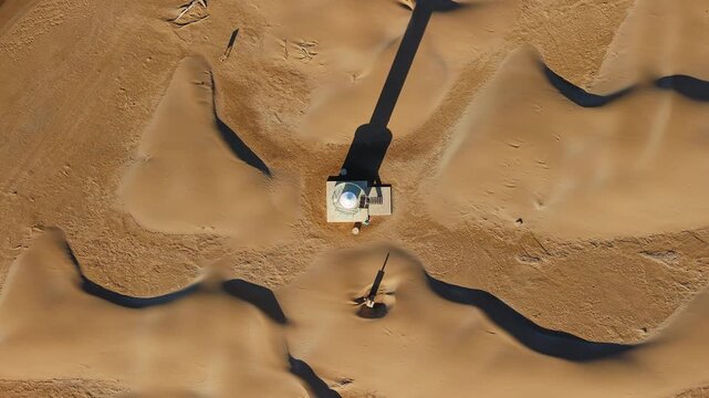 Aerial top down view of lighthouse surrounded by coastal sand dunes at Punta del Fangar in Ebro Delta Natural Park, Spain. Drone ascending vertically above remote beacon and desert