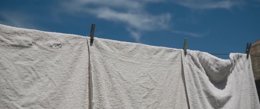 White old worn towel sheets hang on a clothesline, billowing gently in the breeze beneath a clear blue sky, 4K.