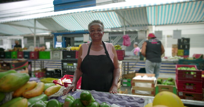 African American elderly woman smiling at outdoor produce market in close portrait expressing warmth life experience and quiet pride within neighborhood street food commerce