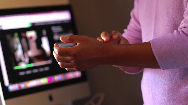 Black woman video editor massaging painful wrist due to carpal tunnel syndrome, repetitive strain injury, or arthritis after working long hours at the computer
