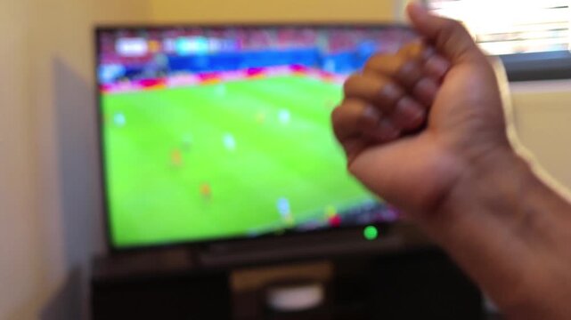 Frustrated soccer fan watching a football game on television, clenching fist in anger and despair over losing team's performance during a major league championship match