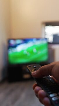 Person changing channels with a remote watching a soccer match on a smart tv, enjoying home entertainment and leisure time while relaxing on the couch in the living room