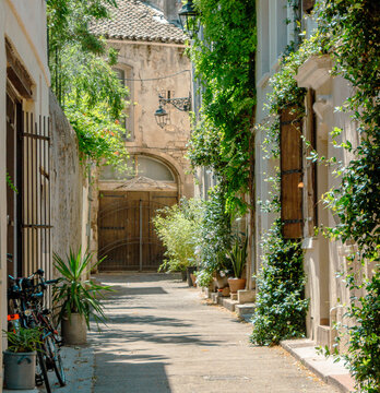 Arles, Provence-Alpes-C&ocirc;te d&rsquo;Azur, France: quiet sunlit alley with plants, shutters and old stone houses. Peaceful Mediterranean street scene in a historic Proven&ccedil;al town.