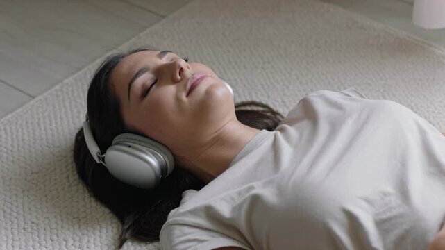 Listening adult woman lying on back on mat, music playing through headphones for rest
