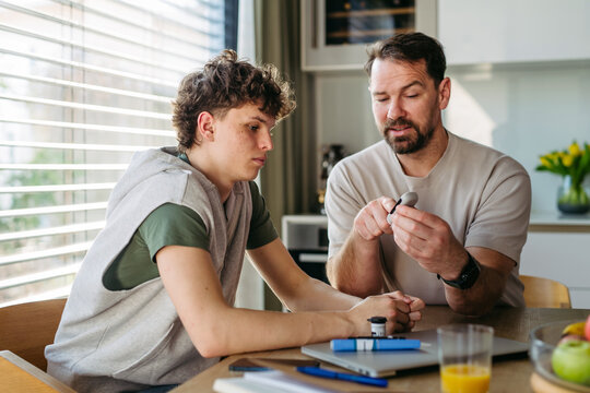 Father checking blood sugar level of diabetic teenage son using glucose meter.