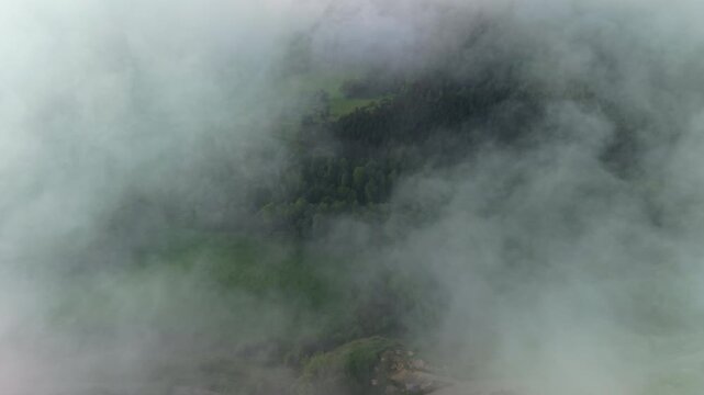 Drone flying through dense mountain clouds toward forested hills in Catalonia, Spain, aerial view of mist drifting over green woodland and countryside landscape