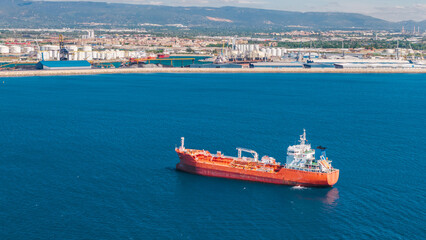 Fototapeta premium Aerial close up of red industrial tanker ship near Tarragona commercial port and refinery facilities in Spain