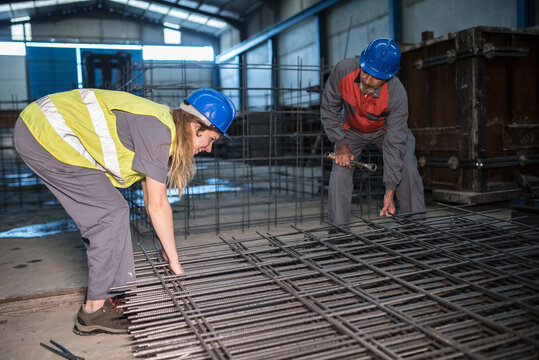Mature worker helps woman to cut welds of the rebar structure checking its hardness.