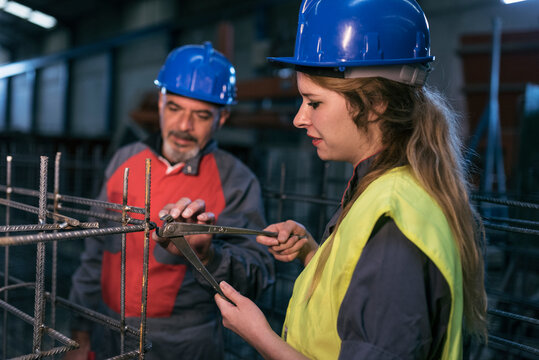 Mature worker helps woman to cut welds of the rebar structure checking its hardness.