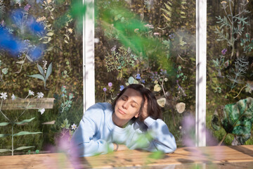Naklejka premium urban woman rests eyes closed at wooden table near glass with floral drawings. finding peace in nature helps city dweller recharge. true nature connection brings deep calm and relaxation