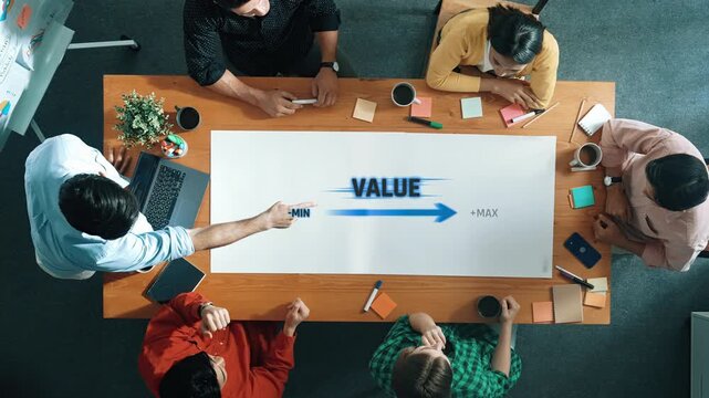 Overhead view of a professional team engaged in a meeting discussing value creation. Participants analyze data trends on a table, incorporating visuals to enhance communication. Raster