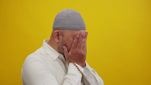 Close-Up of a Muslim Man Holding Tasbih and Wiping His Face After Prayer, Isolated on a Yellow Studio Background, Representing the Completion of Dua, Faith, Gratitude, Islamic Worship, and Spiritual D
