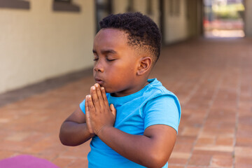 Fototapeta premium African American boy kneeling in tile hall praying in bright-blue-tee near purple mat, copy space